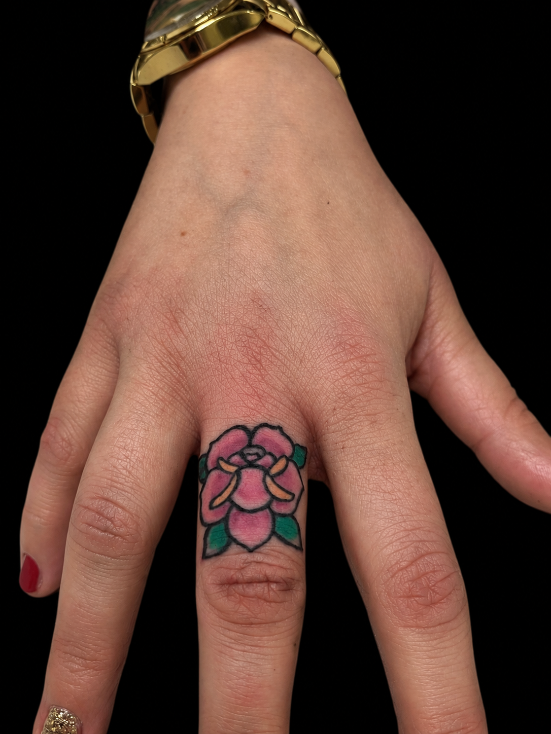 Blüten-Tattoo am Finger, kleine Farbarbeit im traditionellen Stil